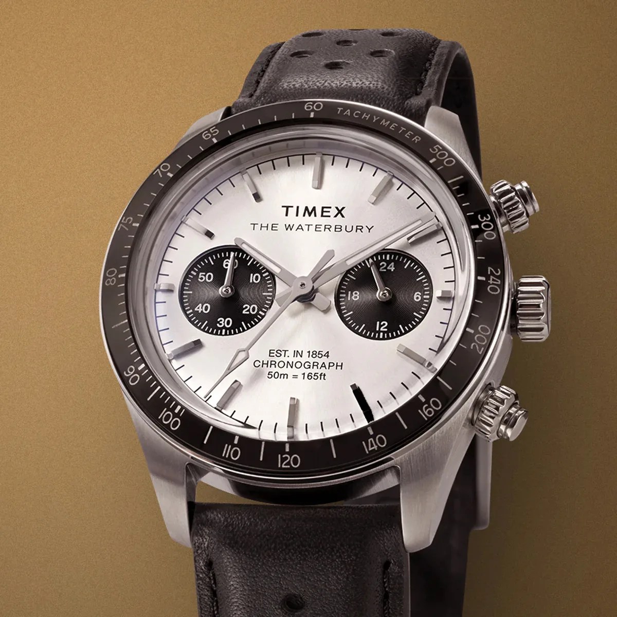 Timex Waterbury chronograph watch with silver dial, black subdials, tachymeter bezel, and black perforated leather strap.