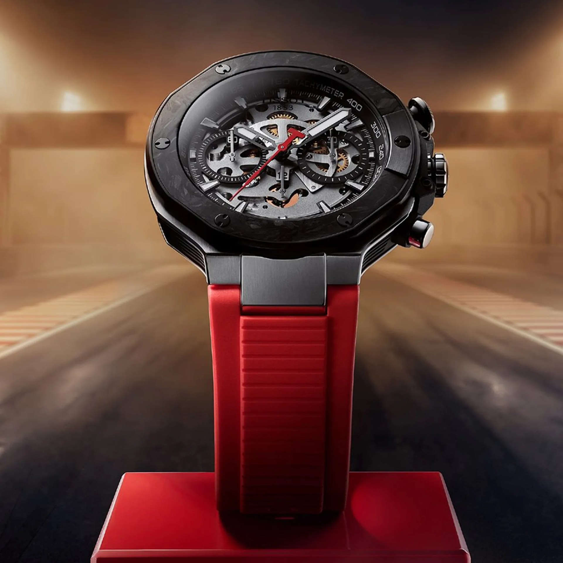 Black watch with visible gears, red second hand, and red rubber strap on a red stand.