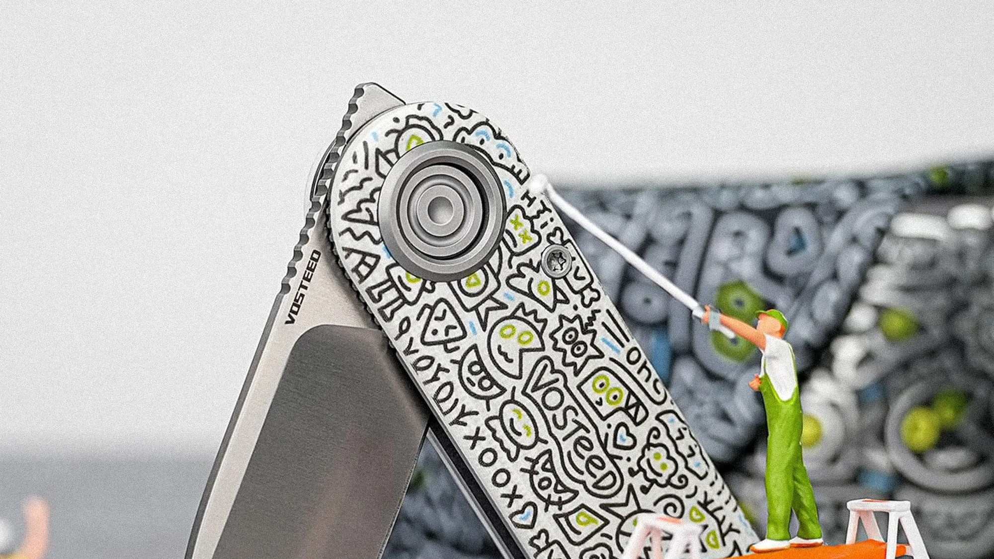 Close-up of a Vosteed folding knife with a doodle-style design on the handle and a miniature figure painting it white.