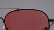 Close-up of black metal-framed sunglasses with dark red lenses and a small logo on the top right lens.