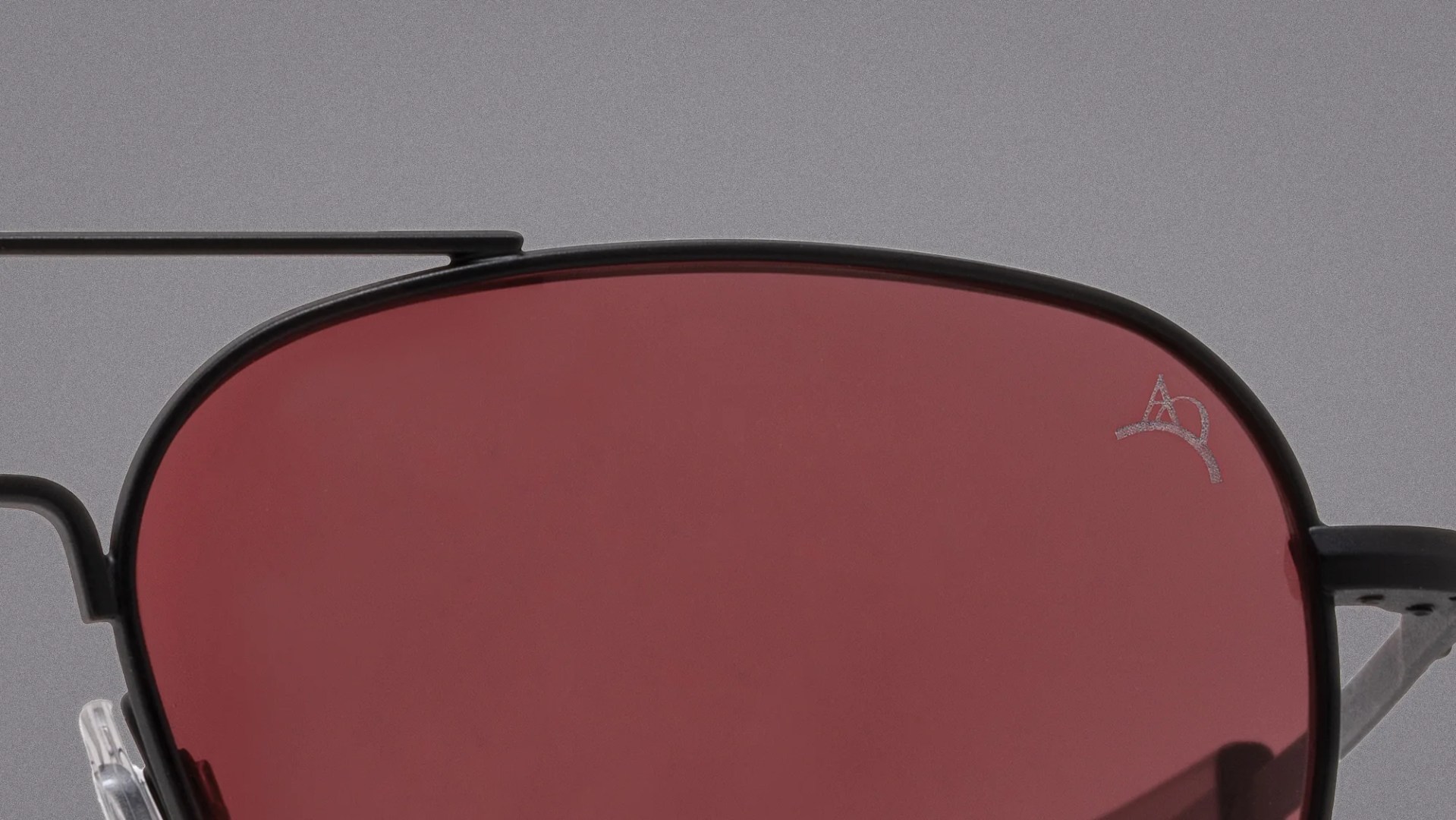 Close-up of black metal-framed sunglasses with dark red lenses and a small logo on the top right lens.