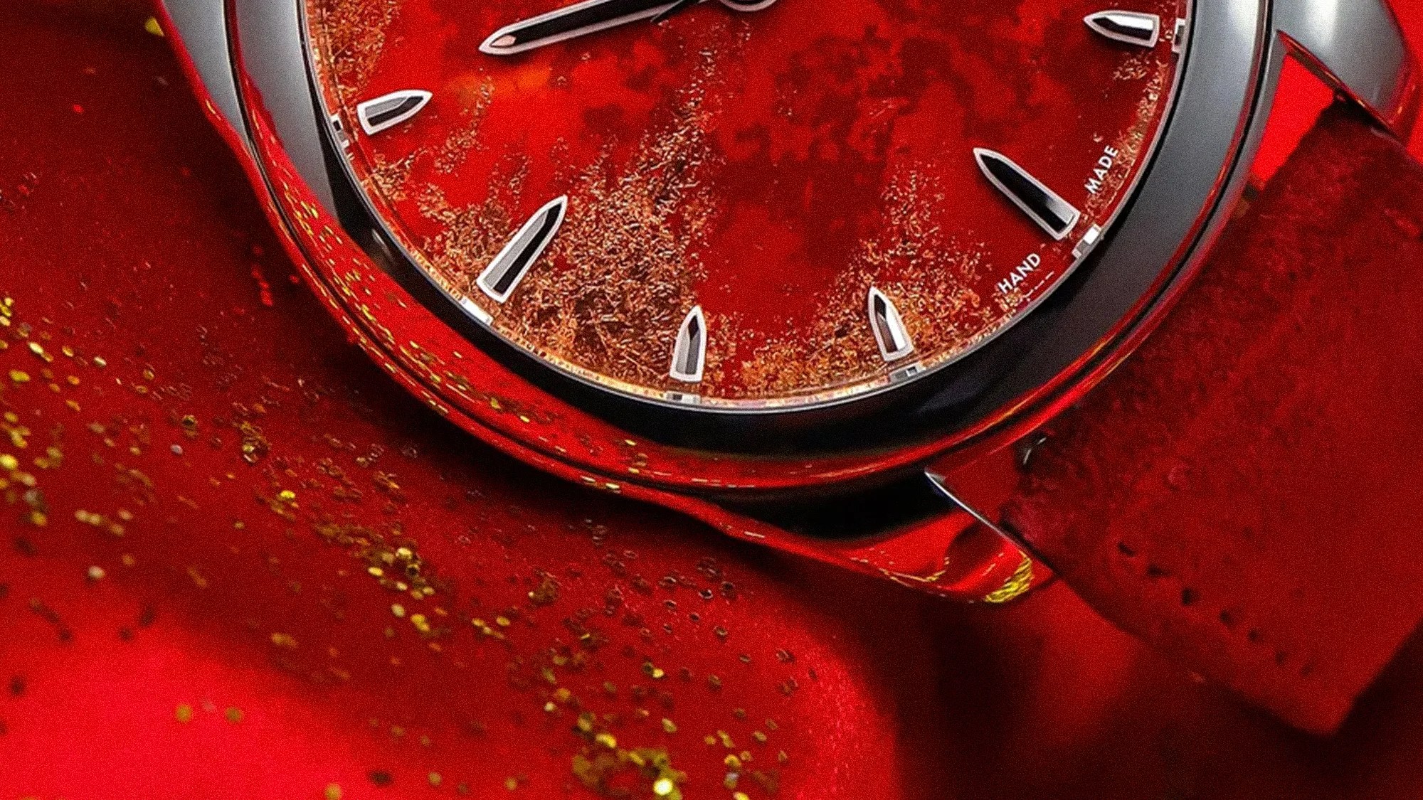 Close-up of a red watch face with silver hour markers and a red leather strap on a red textured surface.