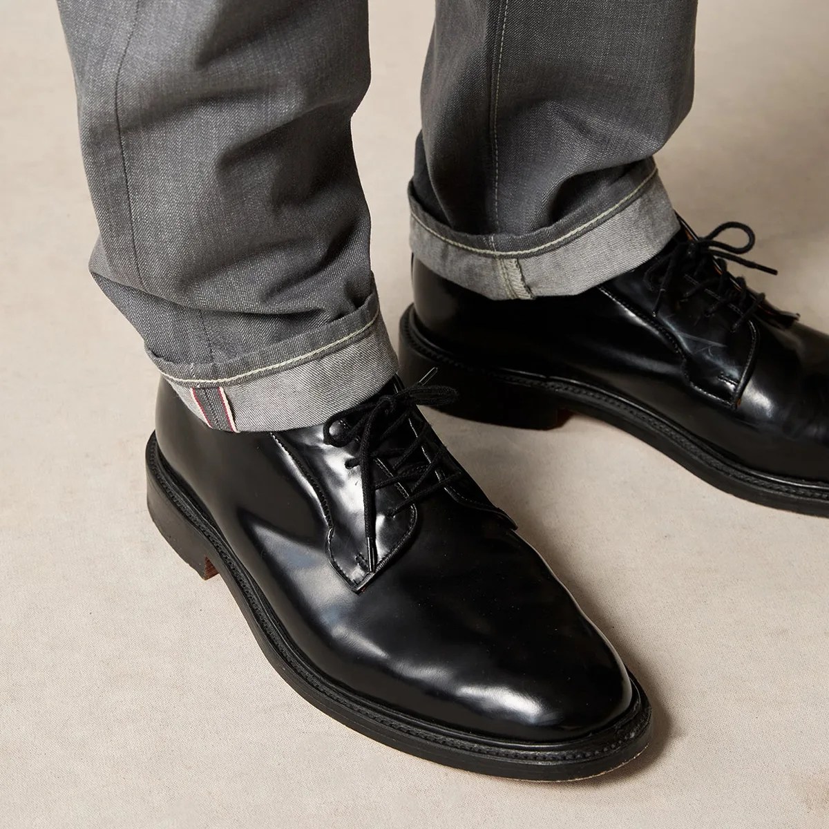 Black polished leather lace-up shoes worn with cuffed gray denim jeans.