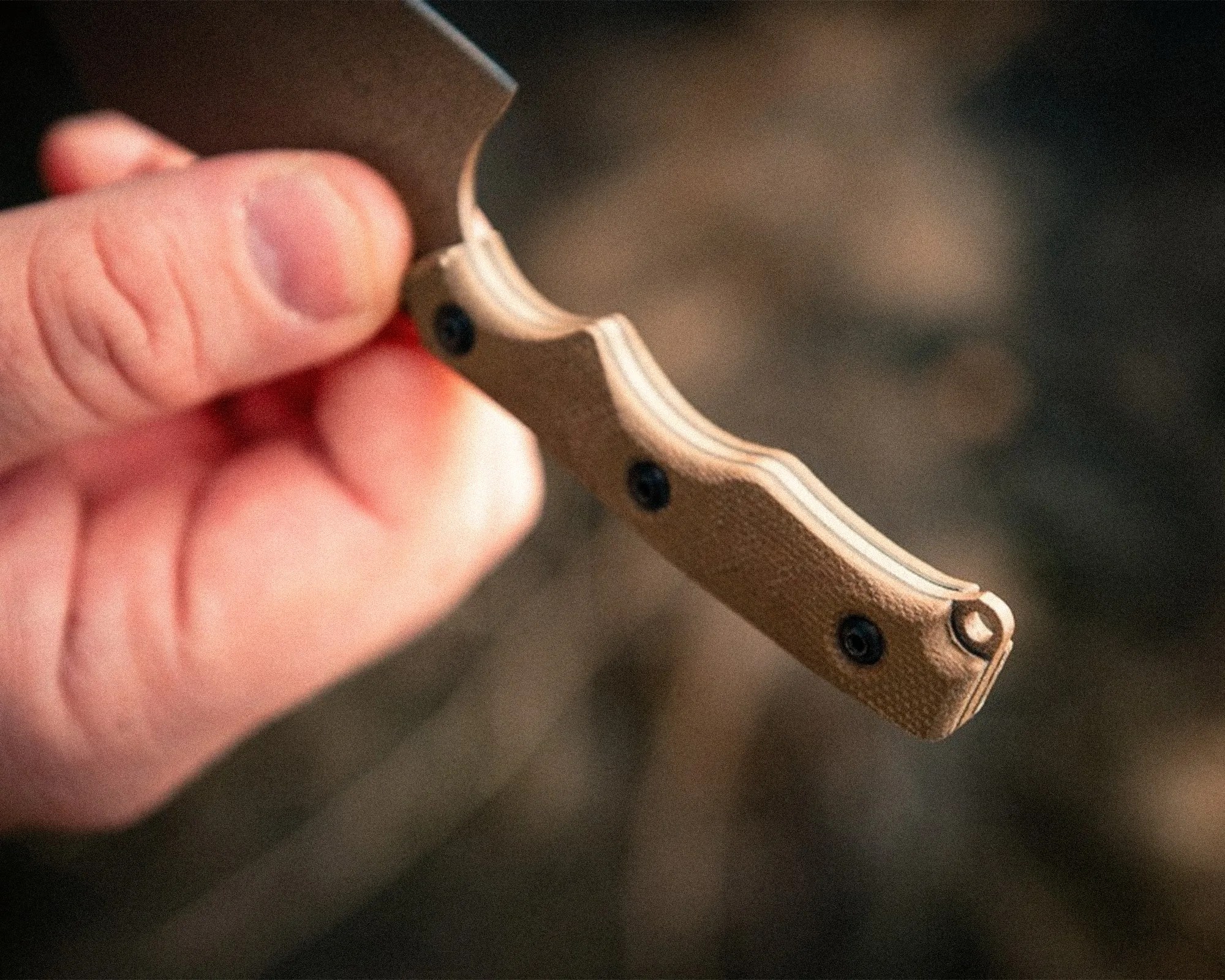 Hand holding a knife with a textured tan handle and black screws.