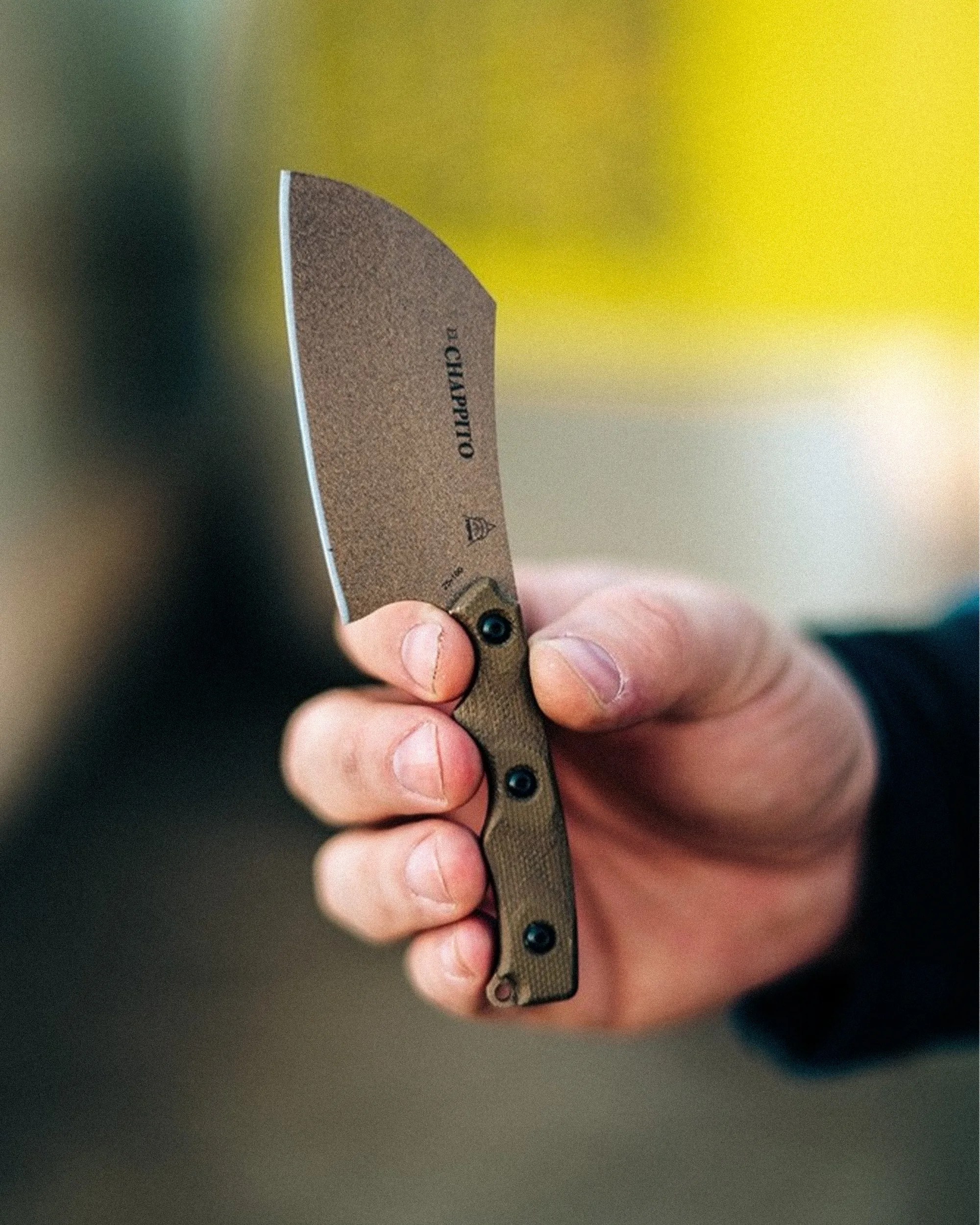 Hand holding a small cleaver-style knife with a textured brown handle and a matte blade.