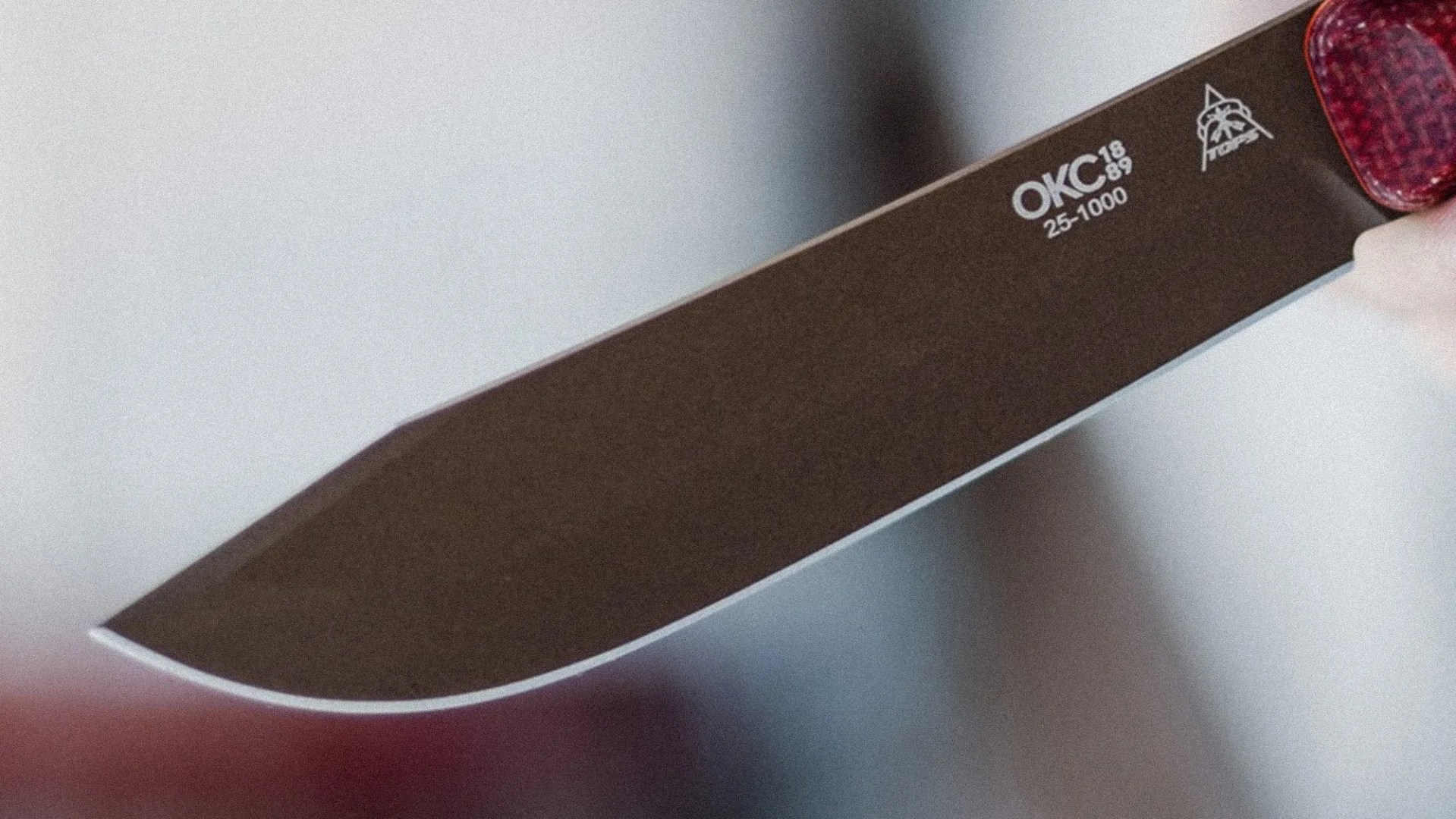 Close-up of a black OKC 25-1000 knife blade with a sharp edge and a red handle.