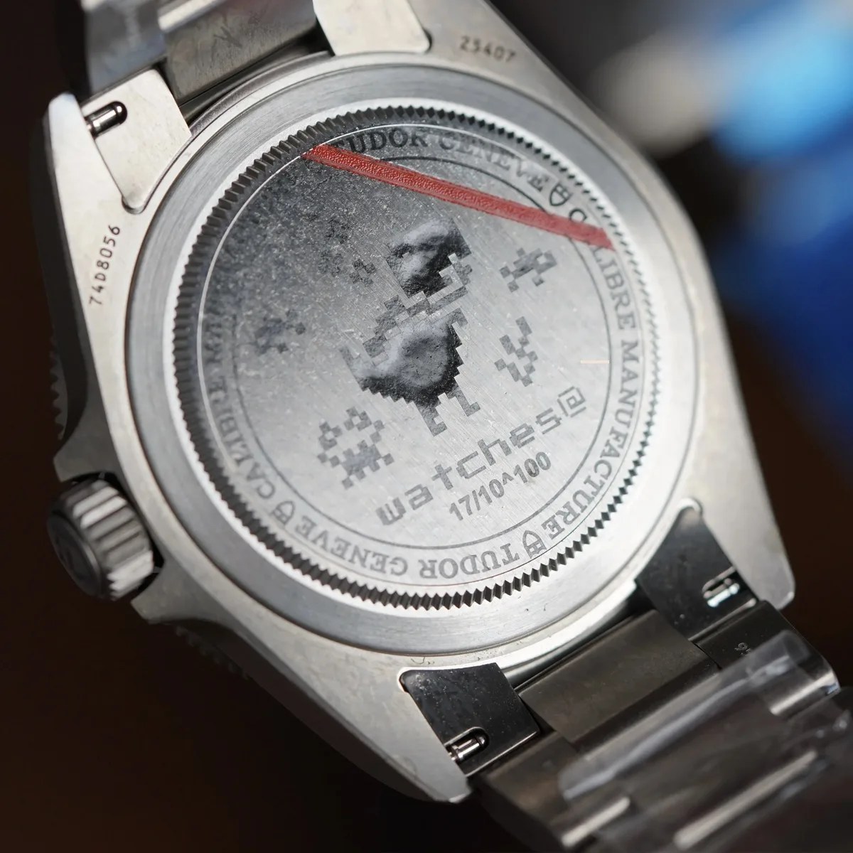 Back of a stainless steel Tudor wristwatch with engraved pixelated design and "watches" text.