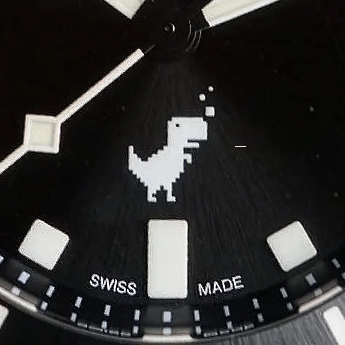 Close-up of a black watch face featuring a pixelated white dinosaur icon above the "Swiss Made" text.