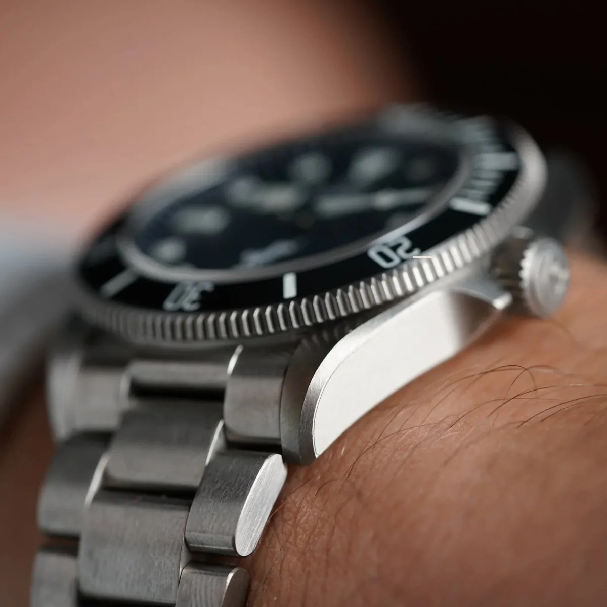Close-up of a stainless steel wristwatch with a black bezel and metal link bracelet on a wrist.