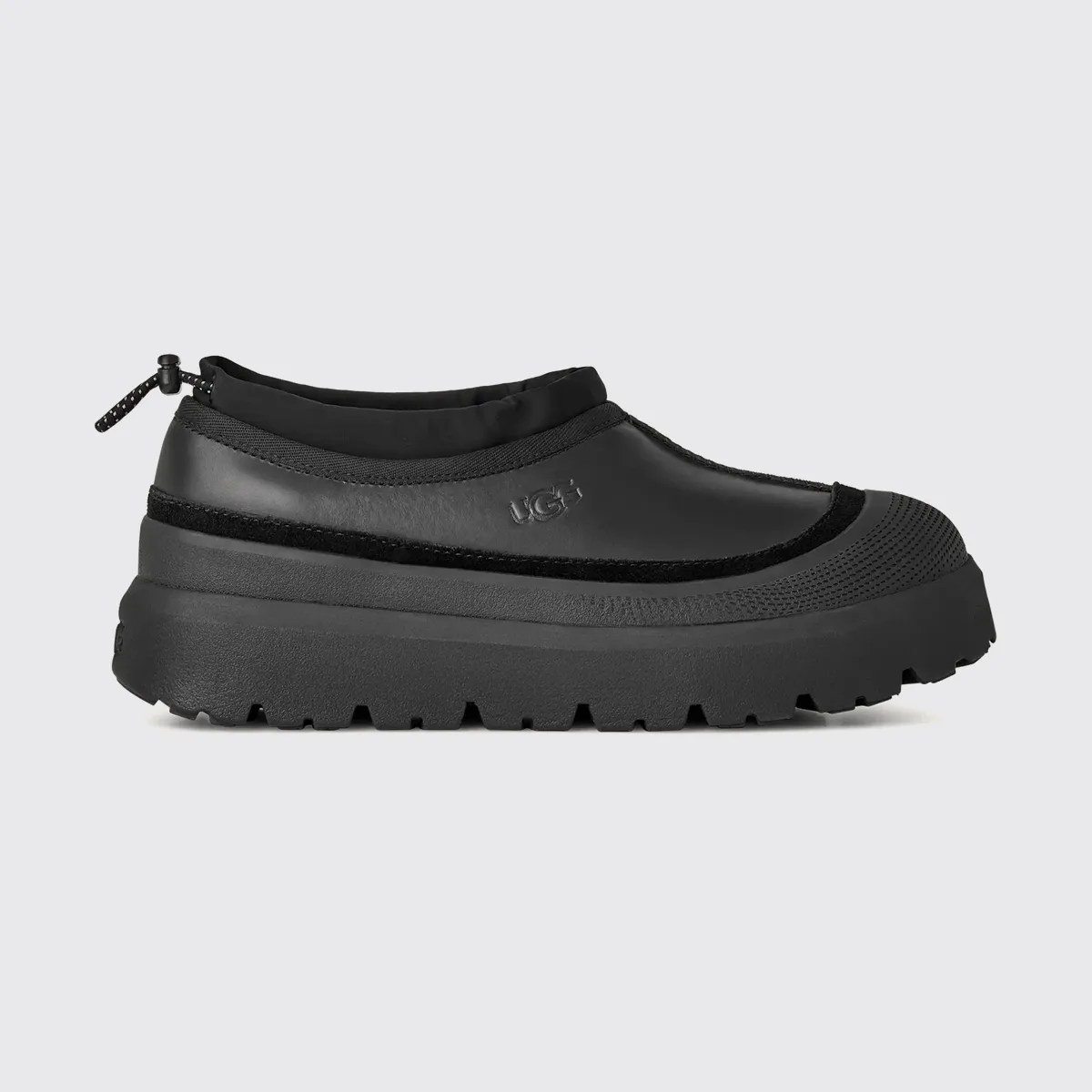 Black slip-on shoe with thick textured sole and UGG logo on the side.