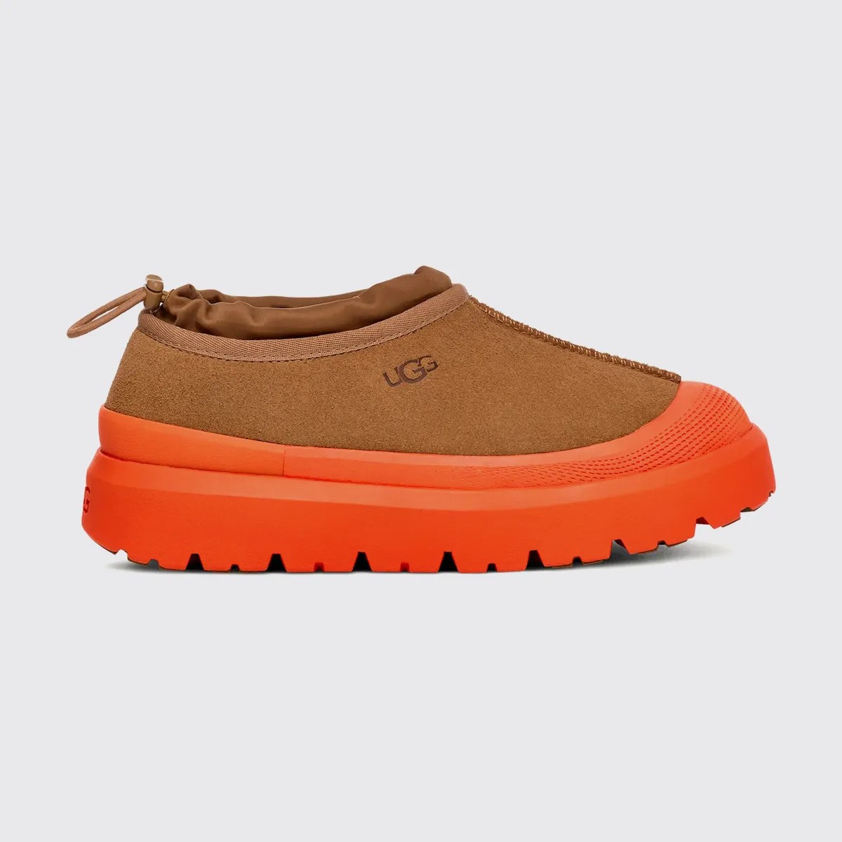 Brown suede slip-on shoe with bright orange thick rubber sole and UGG logo on the side.