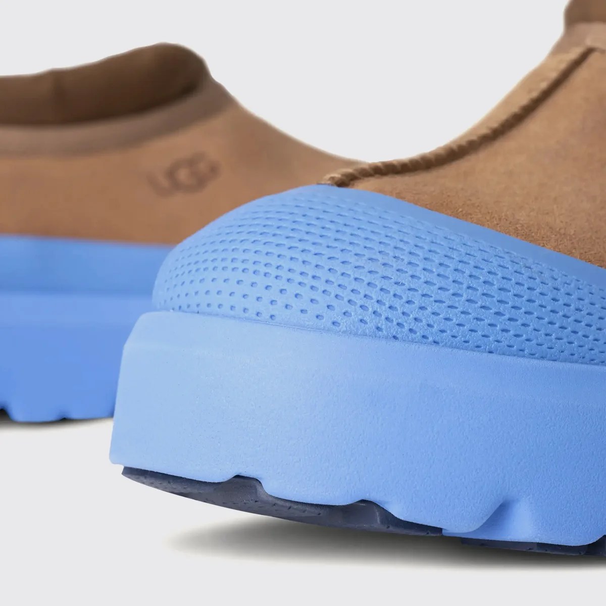 Close-up of brown suede shoes with textured light blue rubber soles and UGG logo on the heel.