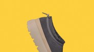Dark gray UGG slip-on shoe with beige chunky sole and adjustable cord on a yellow background.