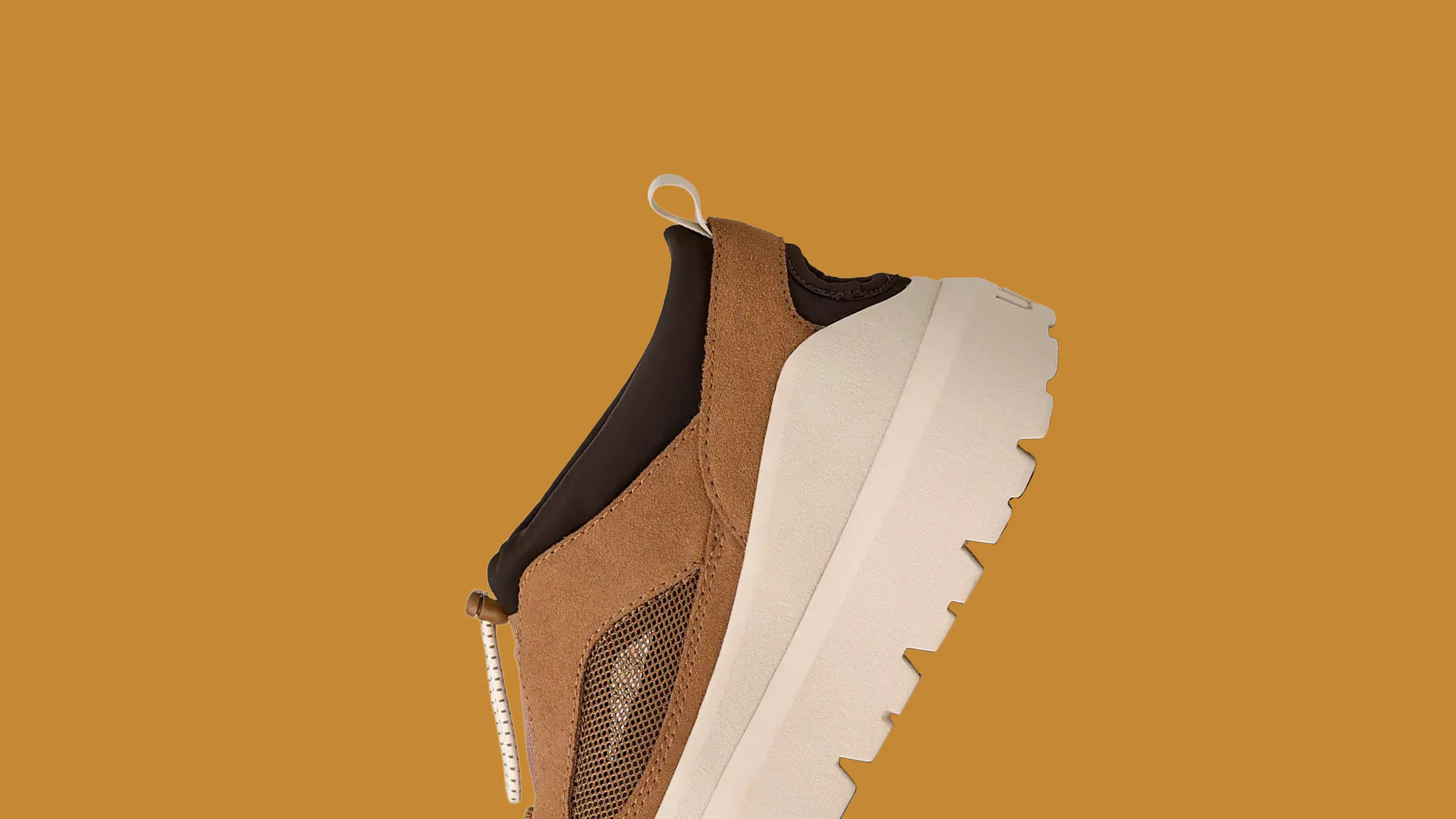 Brown suede and mesh sneaker with thick white sole and black ankle collar on a brown background.