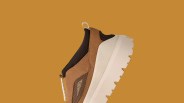 Brown suede and mesh sneaker with thick white sole and black ankle collar on a brown background.