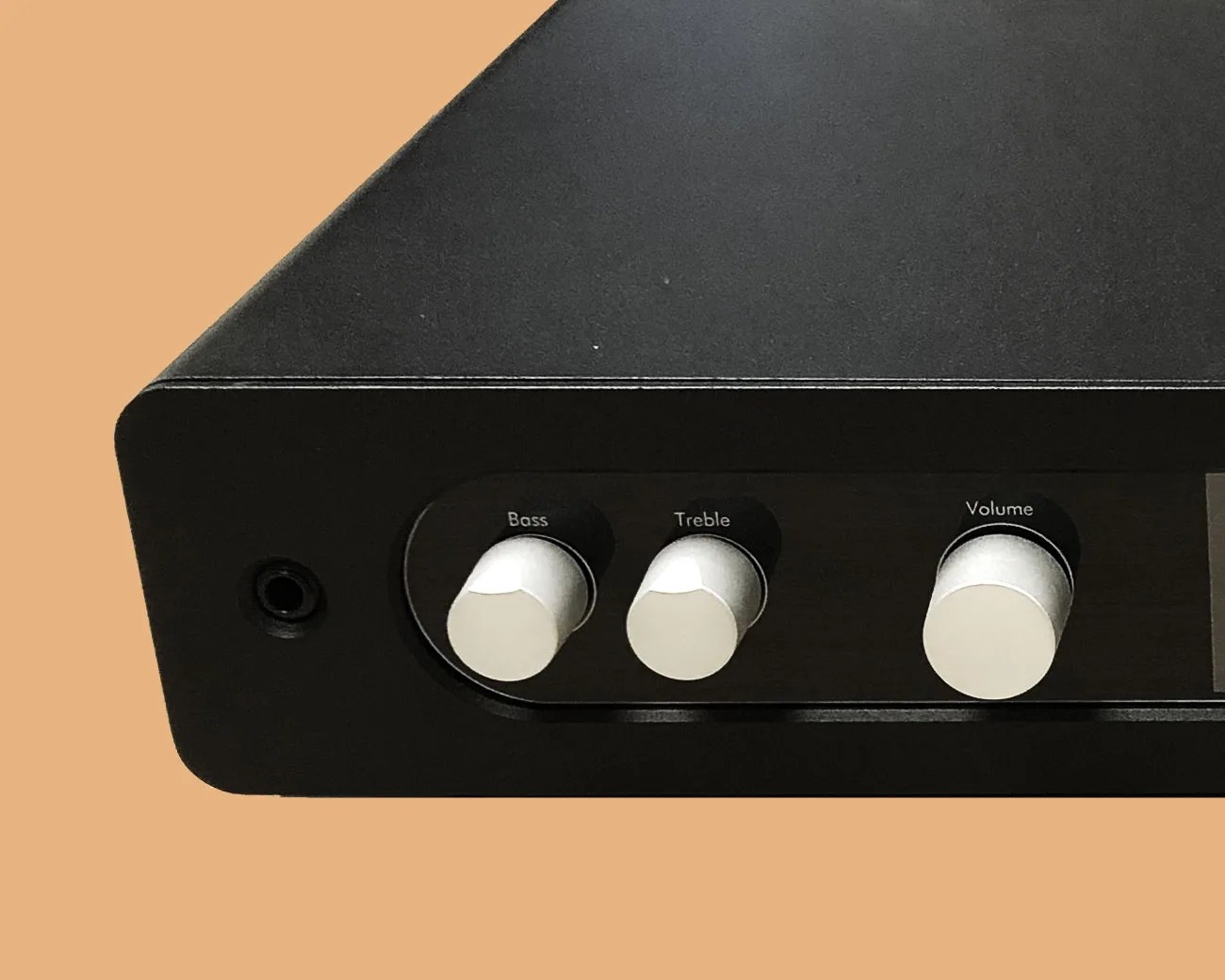 Black audio amplifier with silver knobs labeled Bass, Treble, and Volume on a beige background.