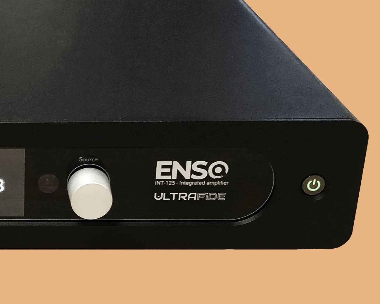 Black Enso INT-125 integrated amplifier with silver source knob and green power button on a tan background.