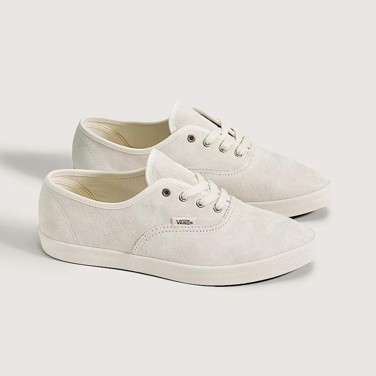 Pair of off-white suede Vans sneakers with white laces and rubber soles on a light background.