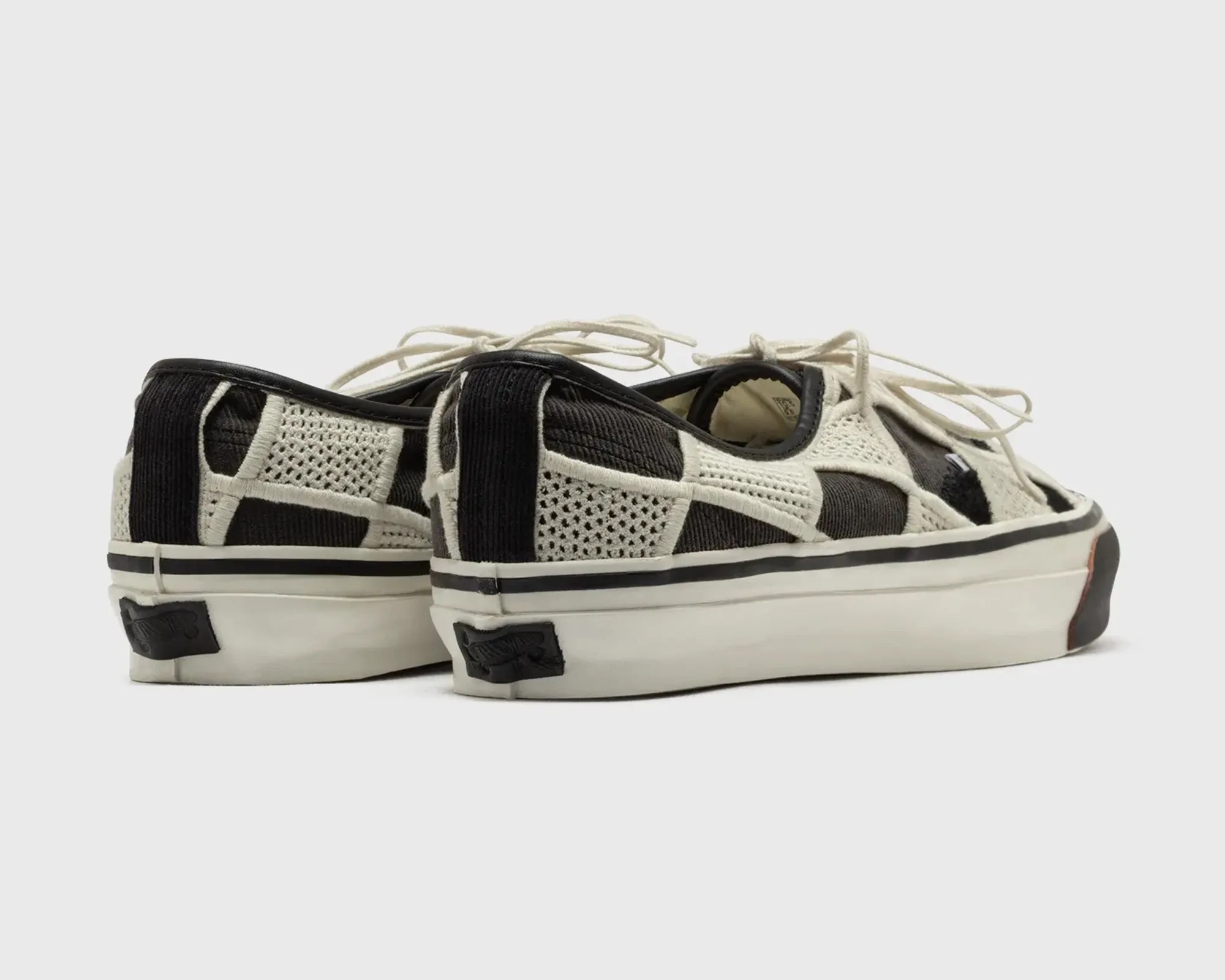 Pair of black and white low-top sneakers with patchwork knit design and white laces on a white background.