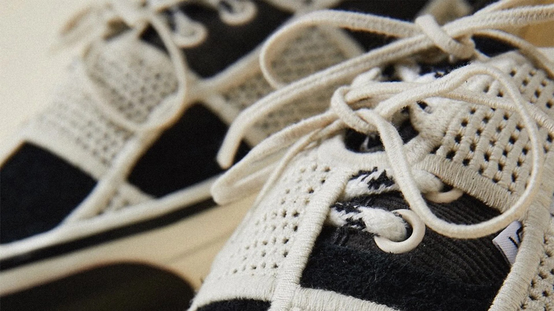 Close-up of black and beige knit sneakers with beige laces and perforated details.