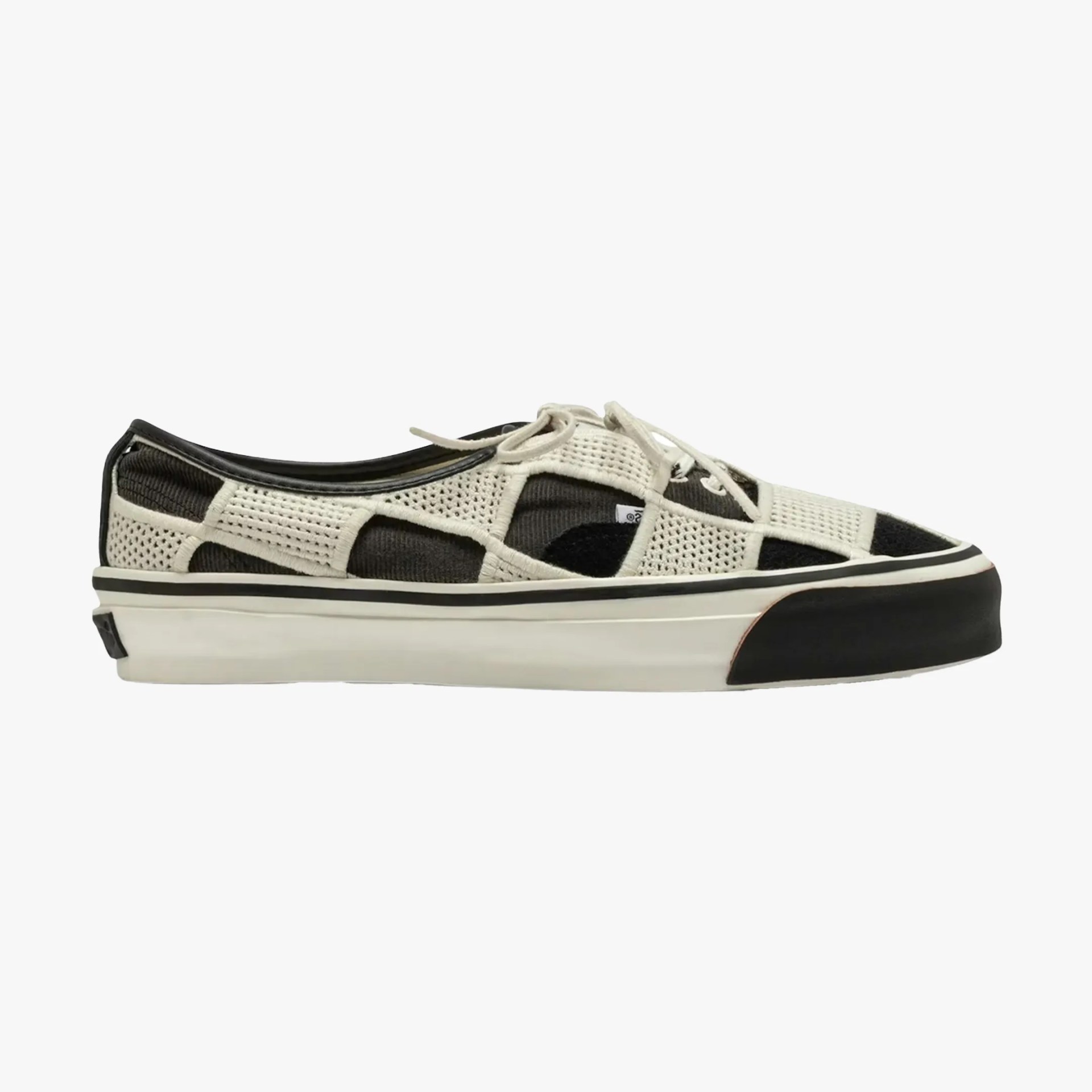 Low-top sneaker with black and white patchwork mesh upper and white rubber sole with black toe cap.
