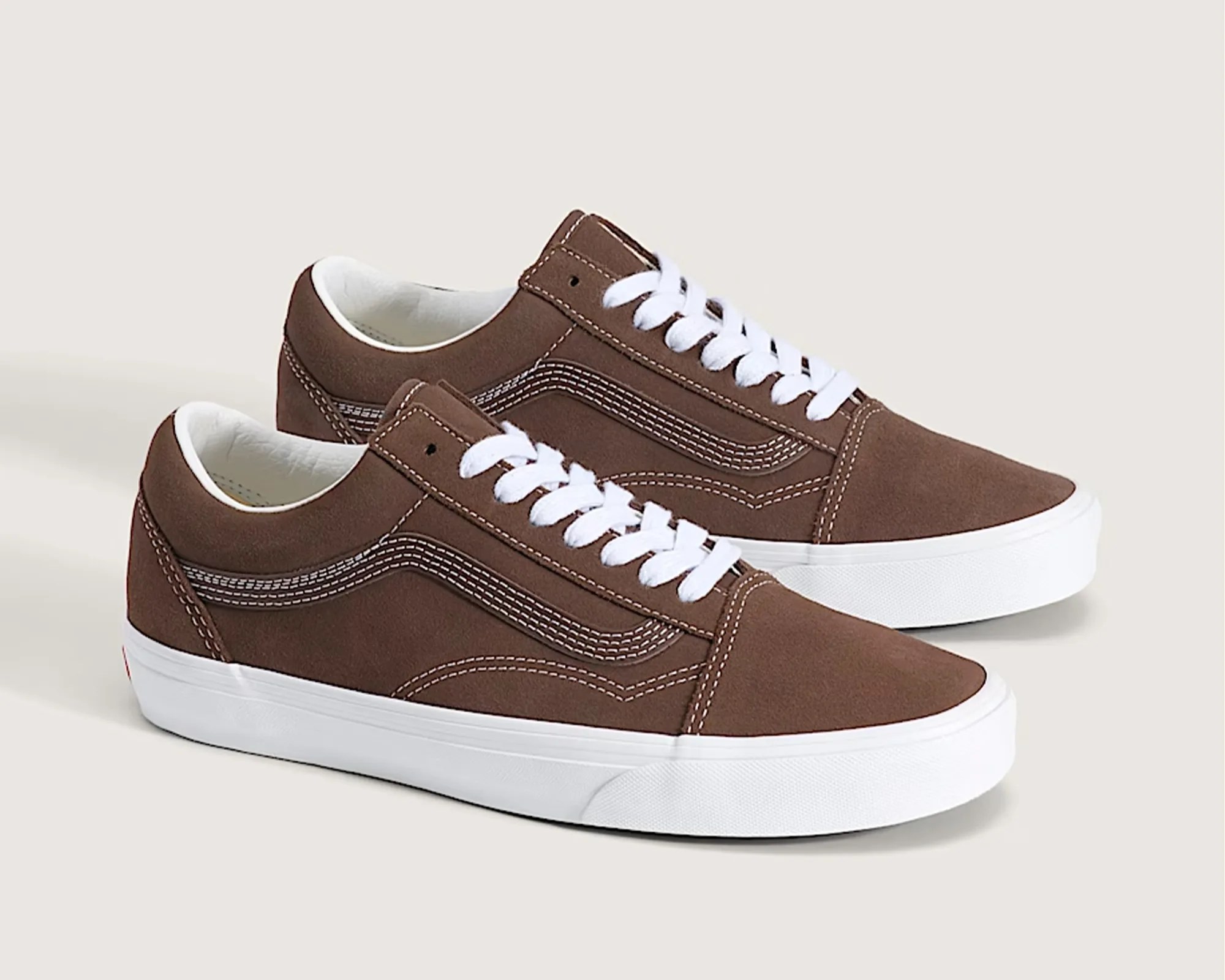 Pair of brown suede low-top sneakers with white laces and thick white rubber soles on a beige background.