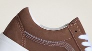 Brown suede sneaker with white stitching and white laces on a light background.