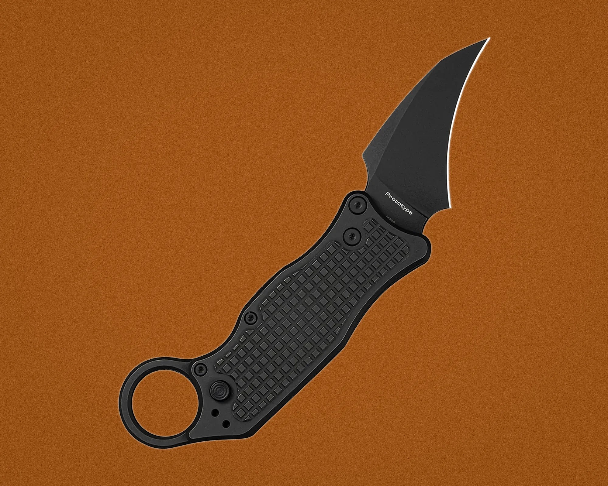 Black folding knife with textured handle and curved blade labeled "Prototype" on a brown background.