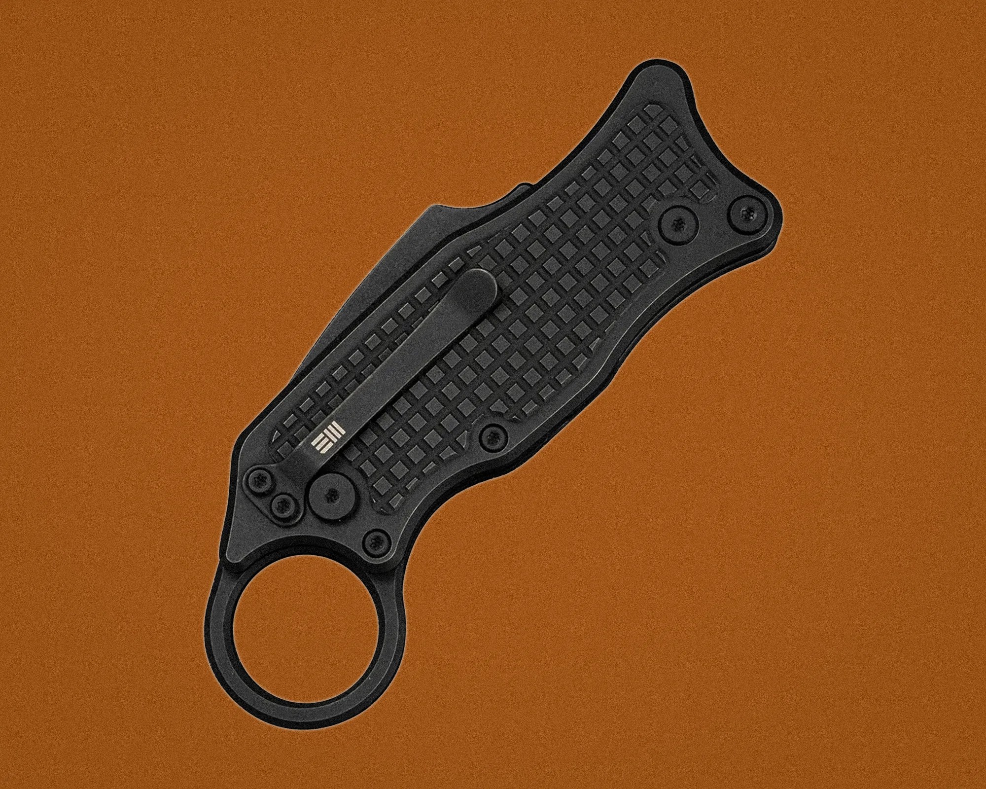 Black folding knife with textured handle and circular finger hole on a brown background.