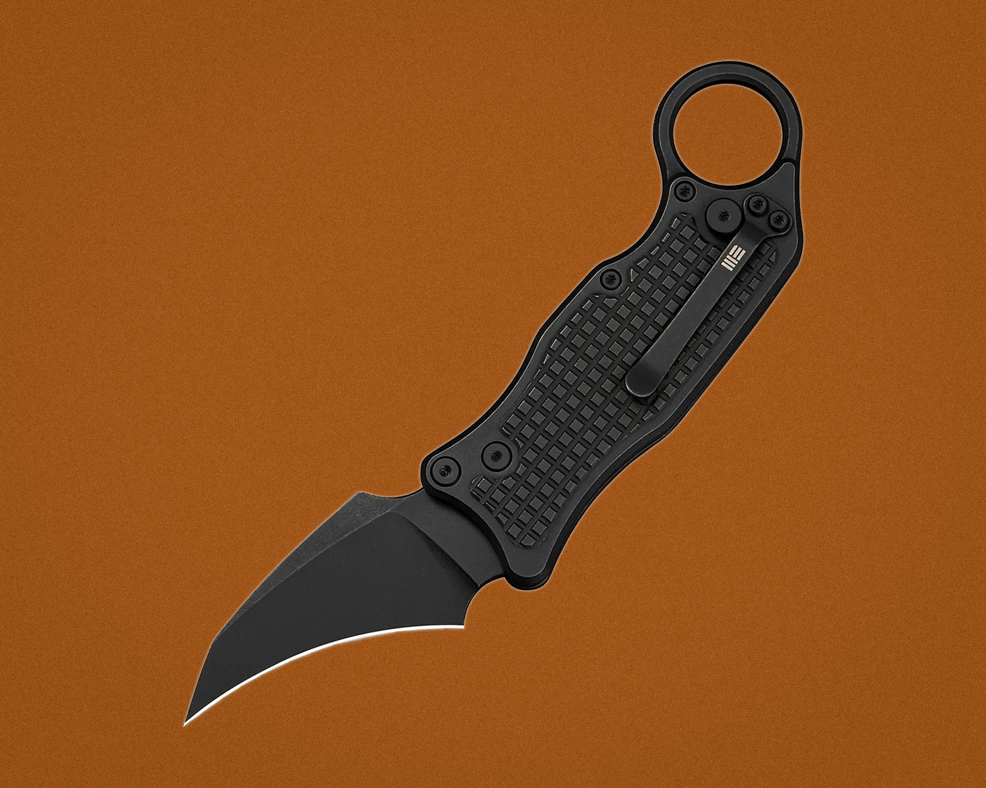 Black folding karambit knife with textured handle and pocket clip on a brown background.
