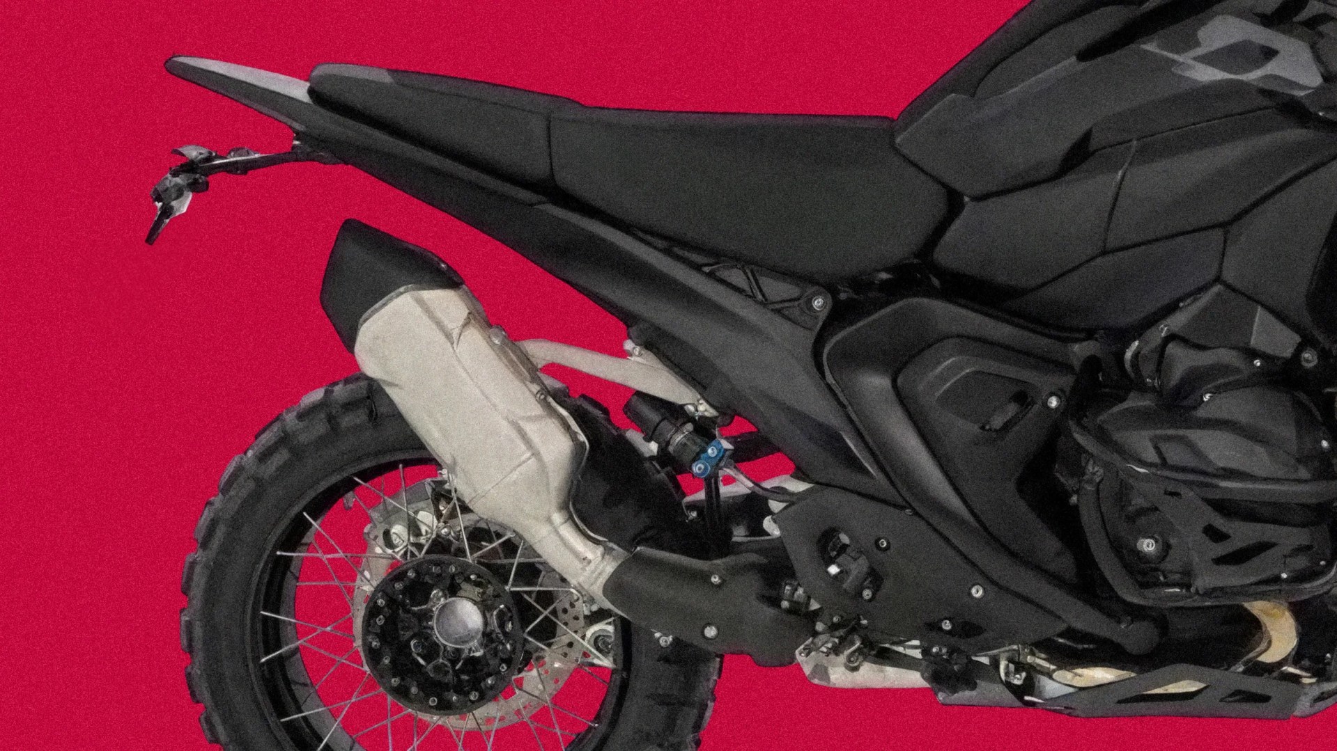 Rear side of a black off-road motorcycle with knobby tire and silver exhaust against a red background.