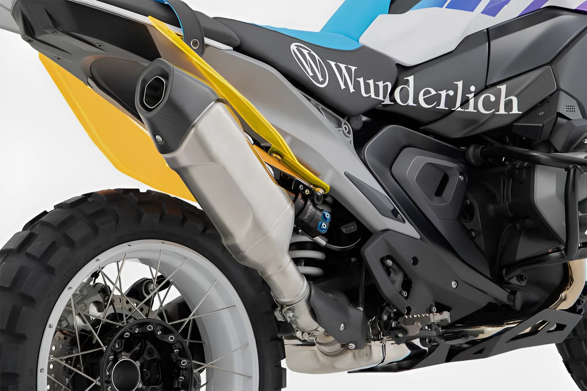 Close-up of a motorcycle's rear wheel, exhaust pipe, and black seat with "Wunderlich" branding.