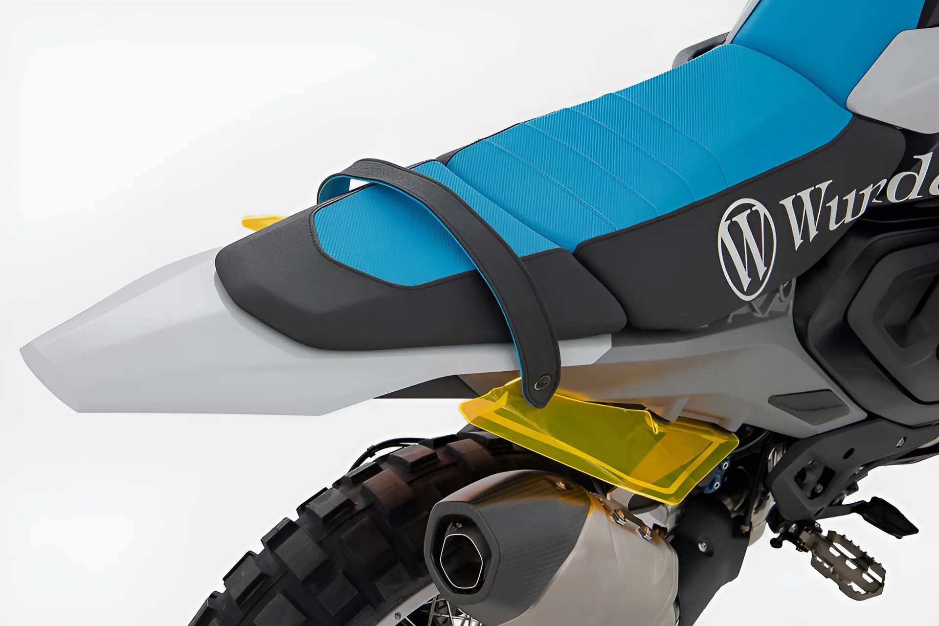 Rear section of a motorcycle with a blue and black seat, knobby tire, and yellow rear fender extension.