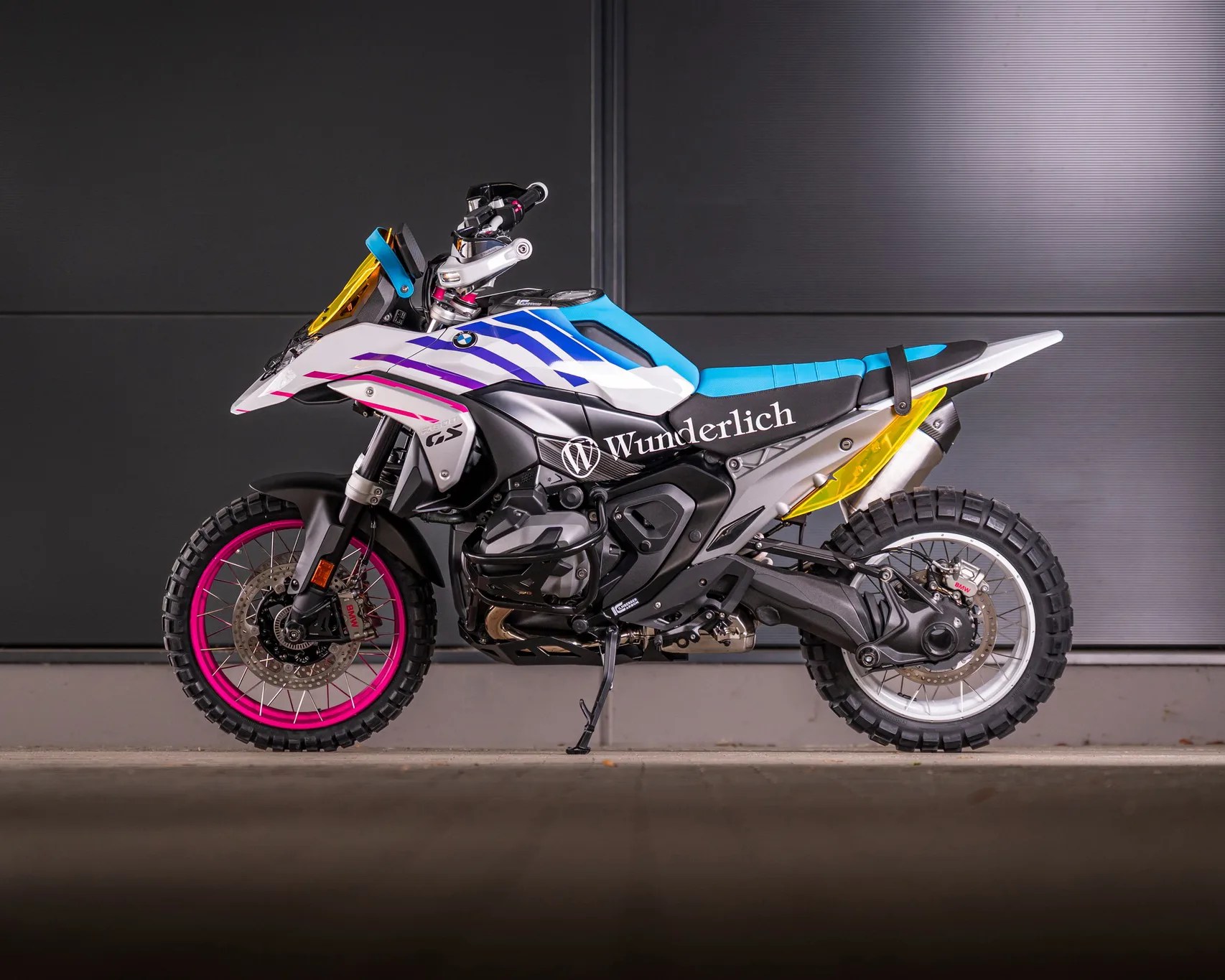 BMW GS adventure motorcycle with pink front wheel rim, blue seat, and Wunderlich branding on the side.