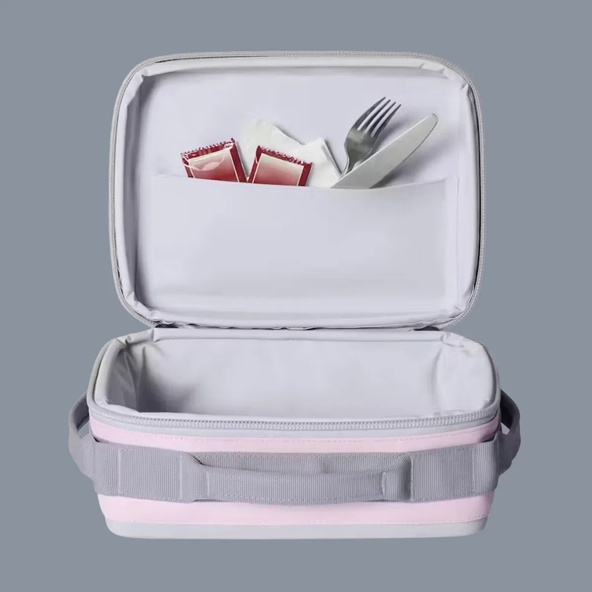 Light pink and gray insulated lunch bag with open lid showing fork, knife, napkin, and ketchup packets in inner pocket.