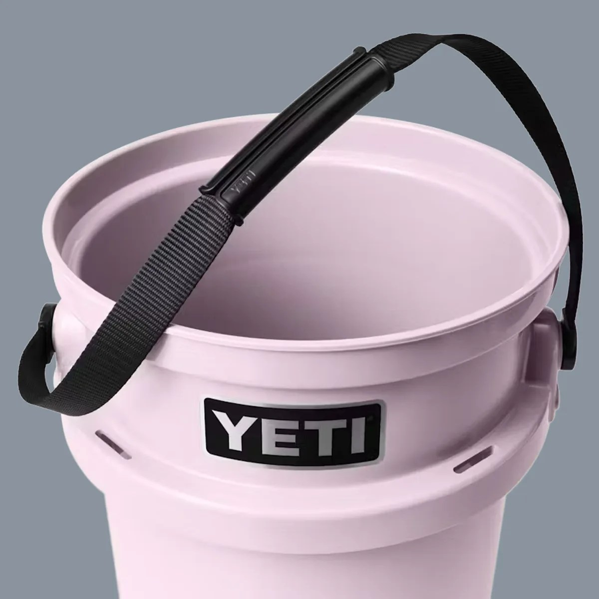 Light pink YETI bucket with black adjustable shoulder strap against a gray background.