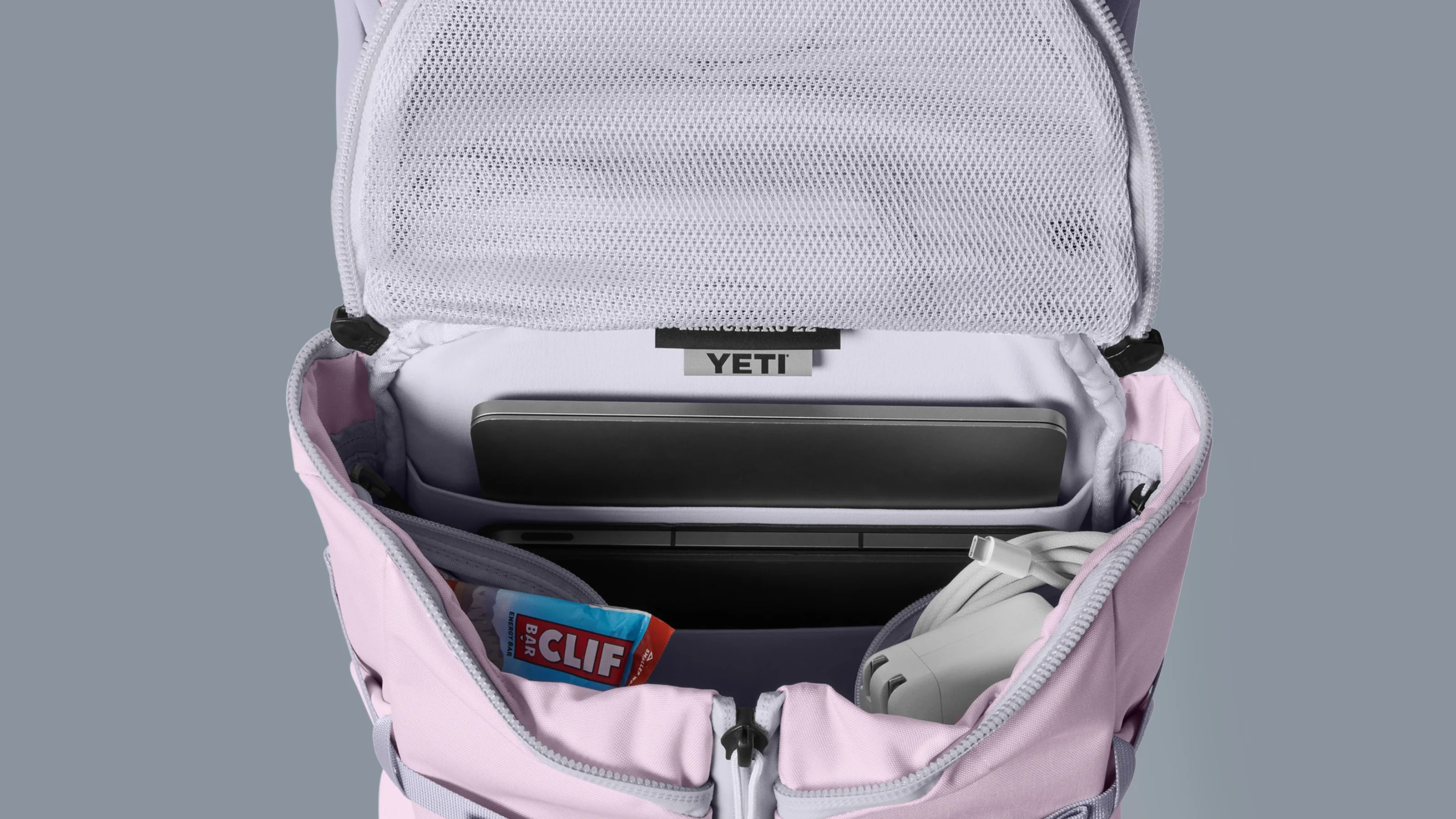 Open light purple YETI backpack showing laptop, charger, and Clif energy bar inside.