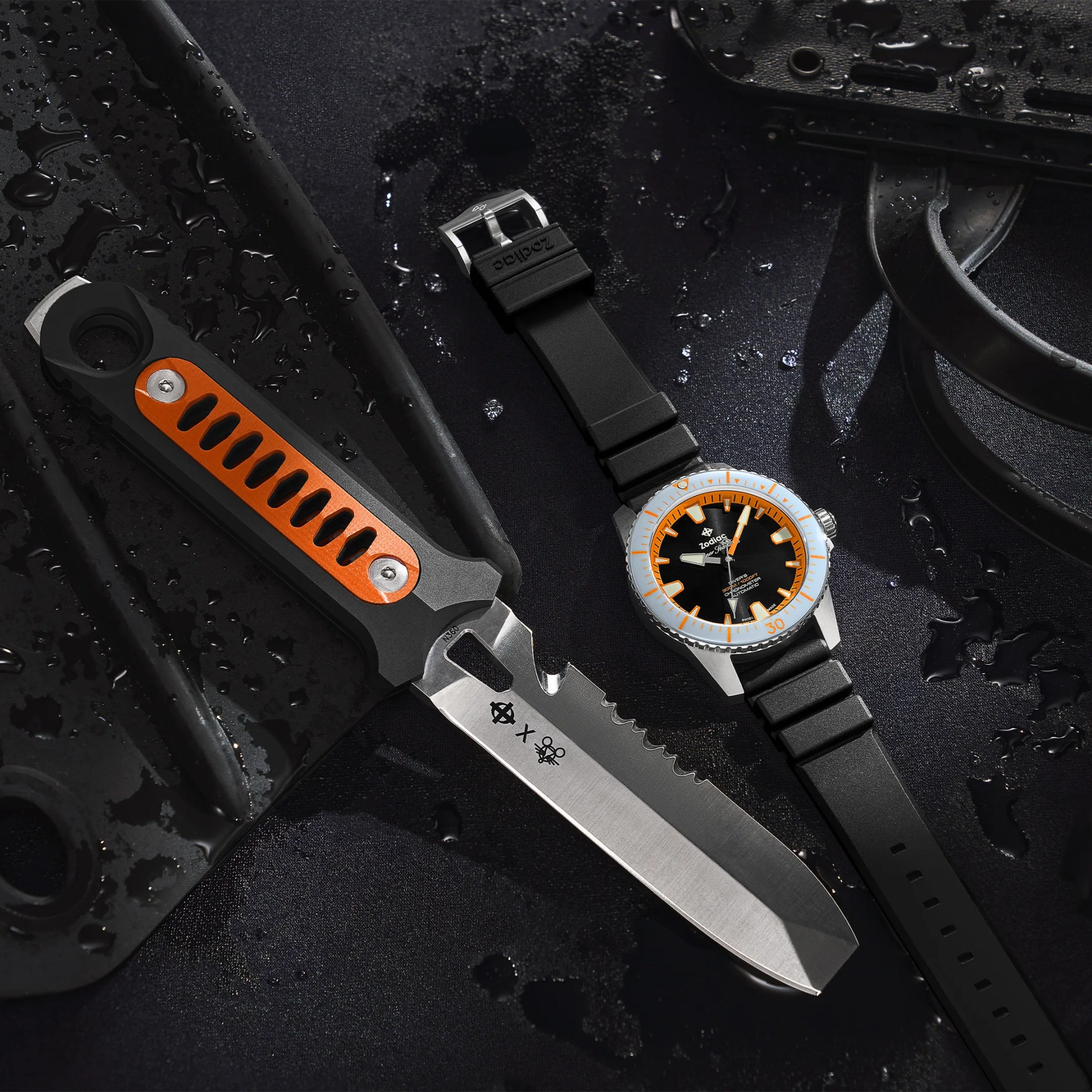 Black and orange dive knife with serrated edge next to a black and orange Zodiac dive watch on a wet surface.