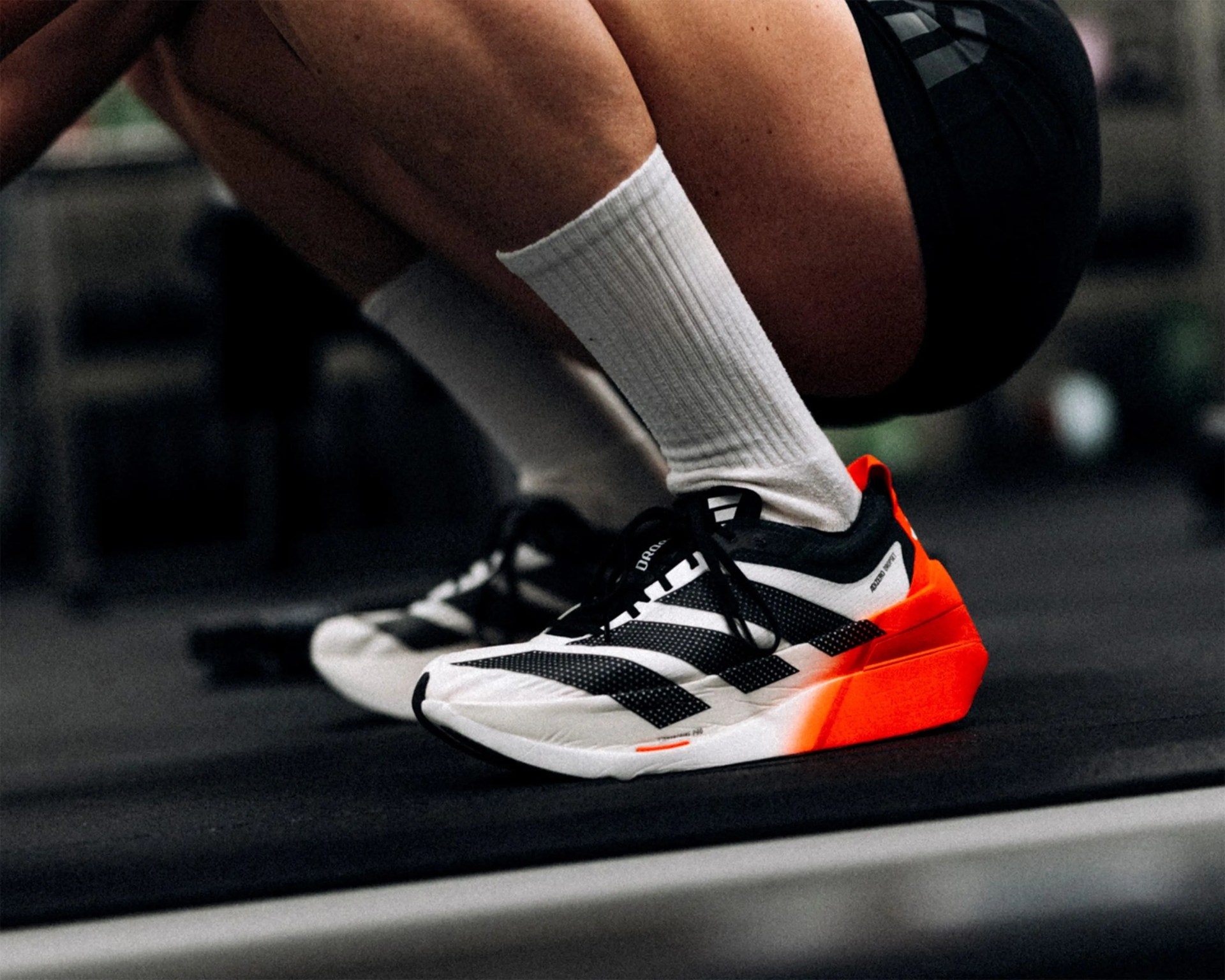 White and black athletic shoes with bright orange heel accents worn with white socks.