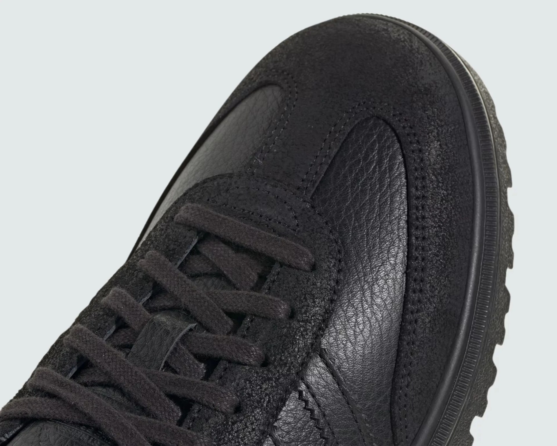 Close-up of a black sneaker toe with textured leather and suede panels and black laces.