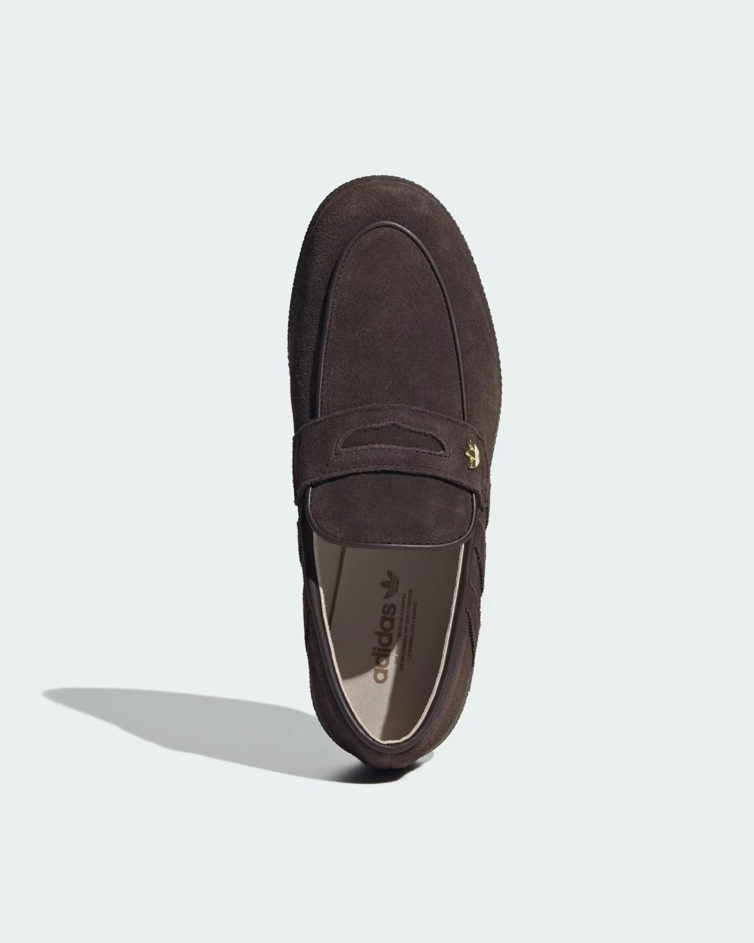 Dark brown suede Adidas loafer with a penny strap and gold emblem on a light background.