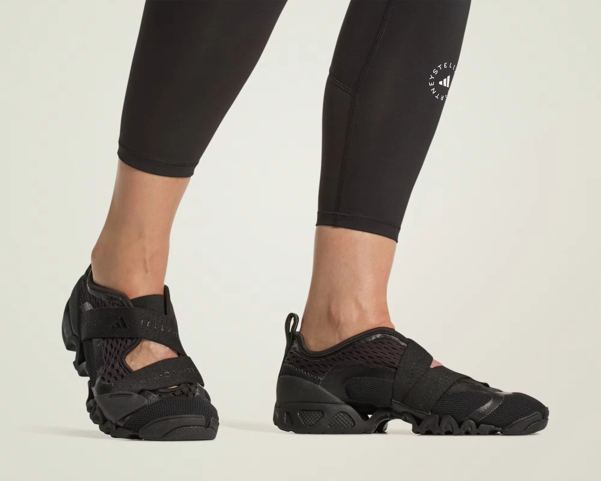 Black mesh and synthetic athletic shoes with elastic straps worn with black cropped leggings.