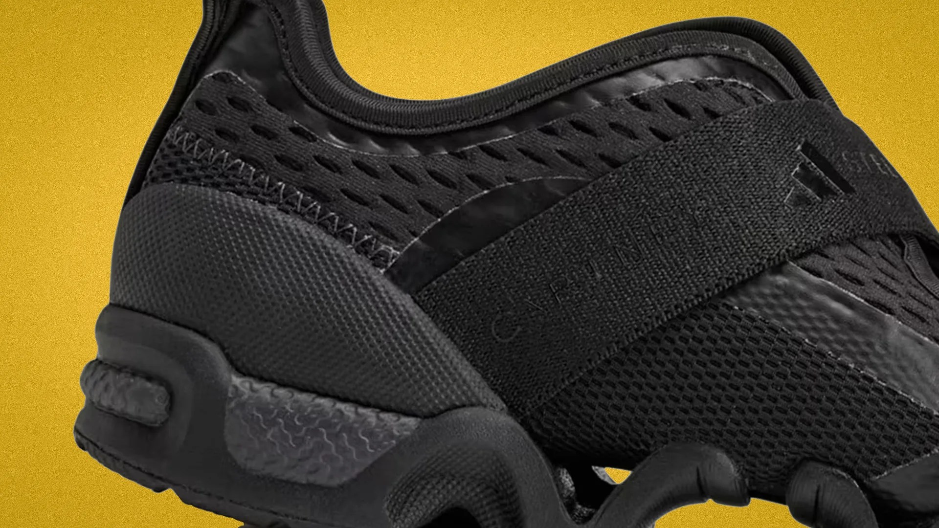 Close-up of a black Adidas sneaker with mesh and textured fabric, featuring a wide strap across the midfoot.