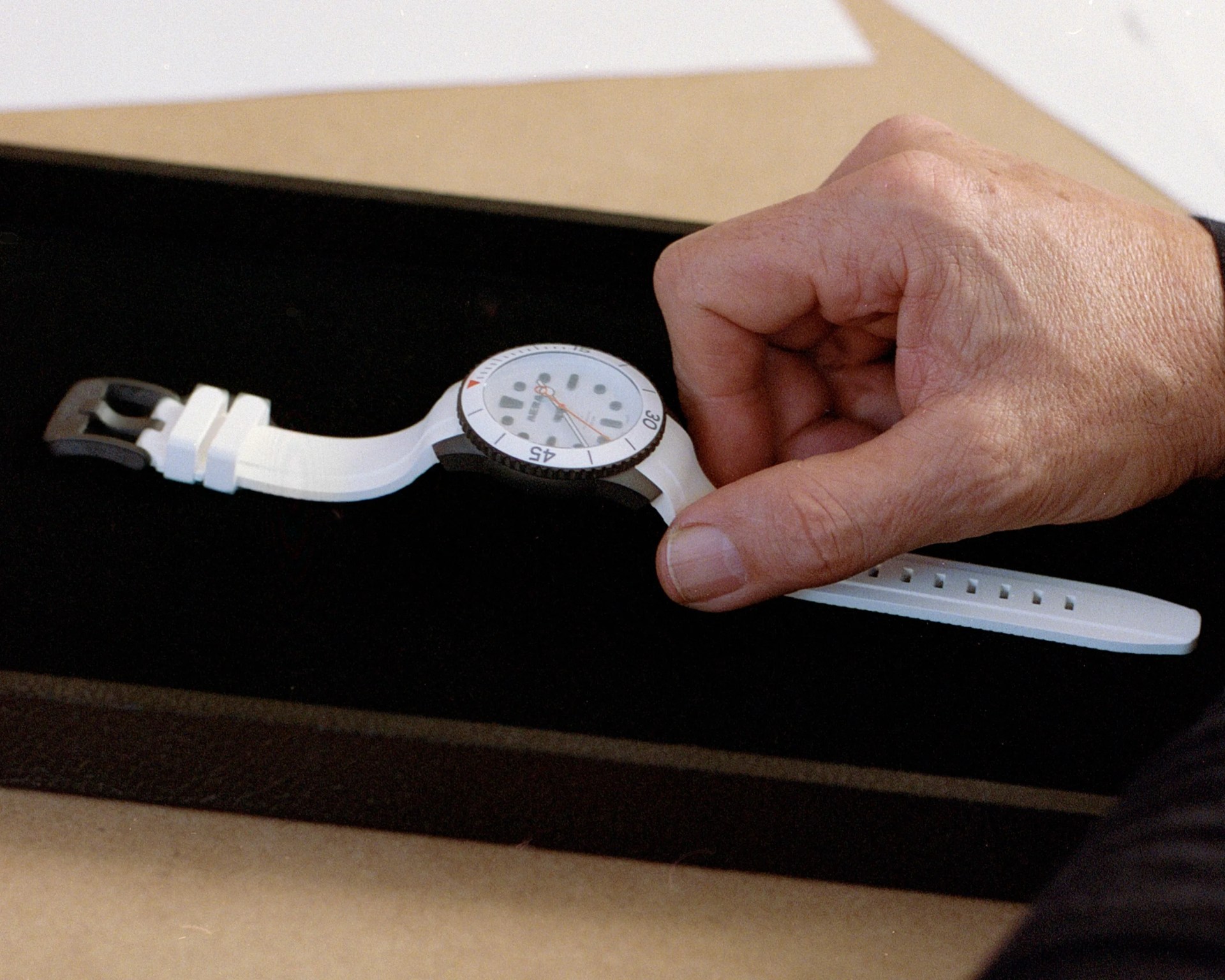 White wristwatch with black bezel and white dial held by a hand over a black surface.