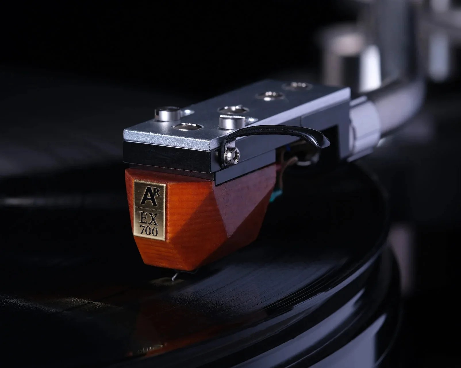 Turntable cartridge with wooden body and metal top labeled "AR EX 700" on a vinyl record.
