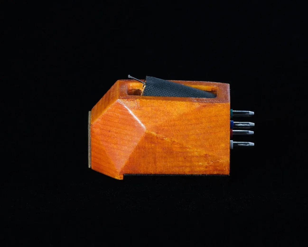Wooden phono cartridge with metal pins and a black stylus on a black background.