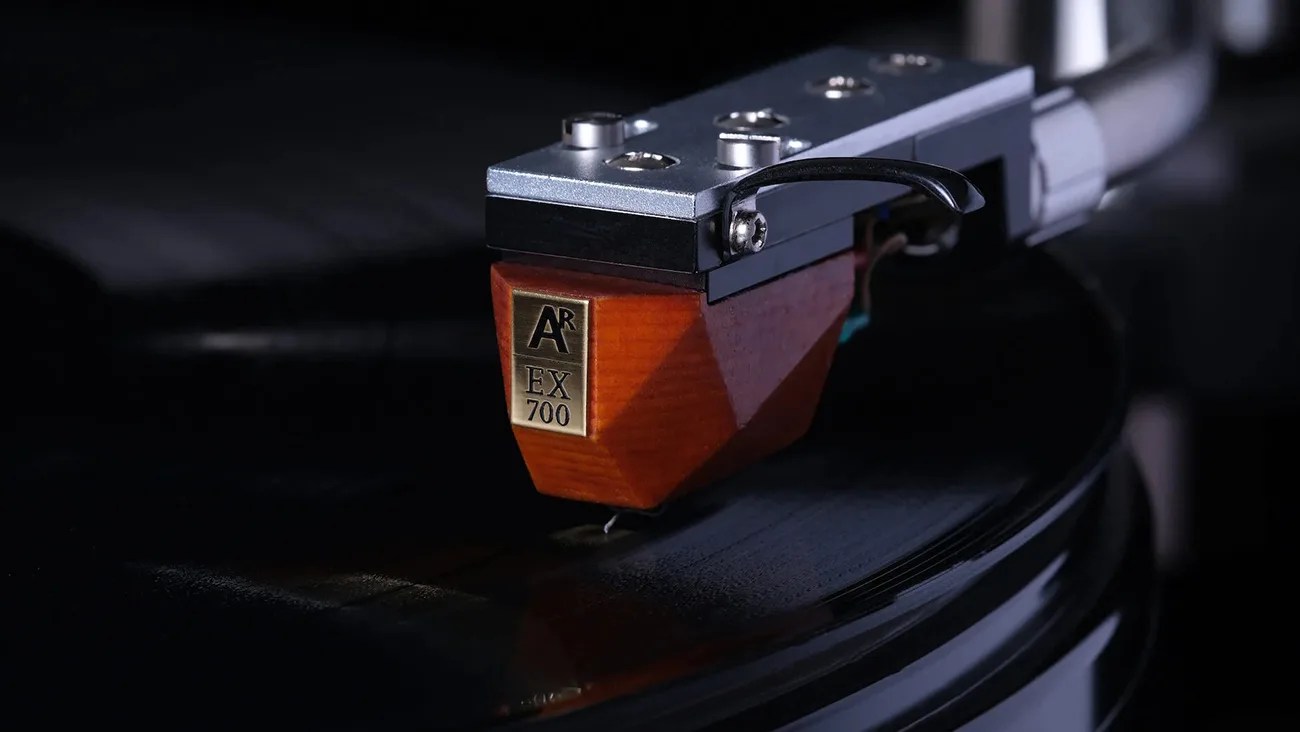 Close-up of a wooden AR EX 700 cartridge mounted on a silver tonearm playing a black vinyl record.