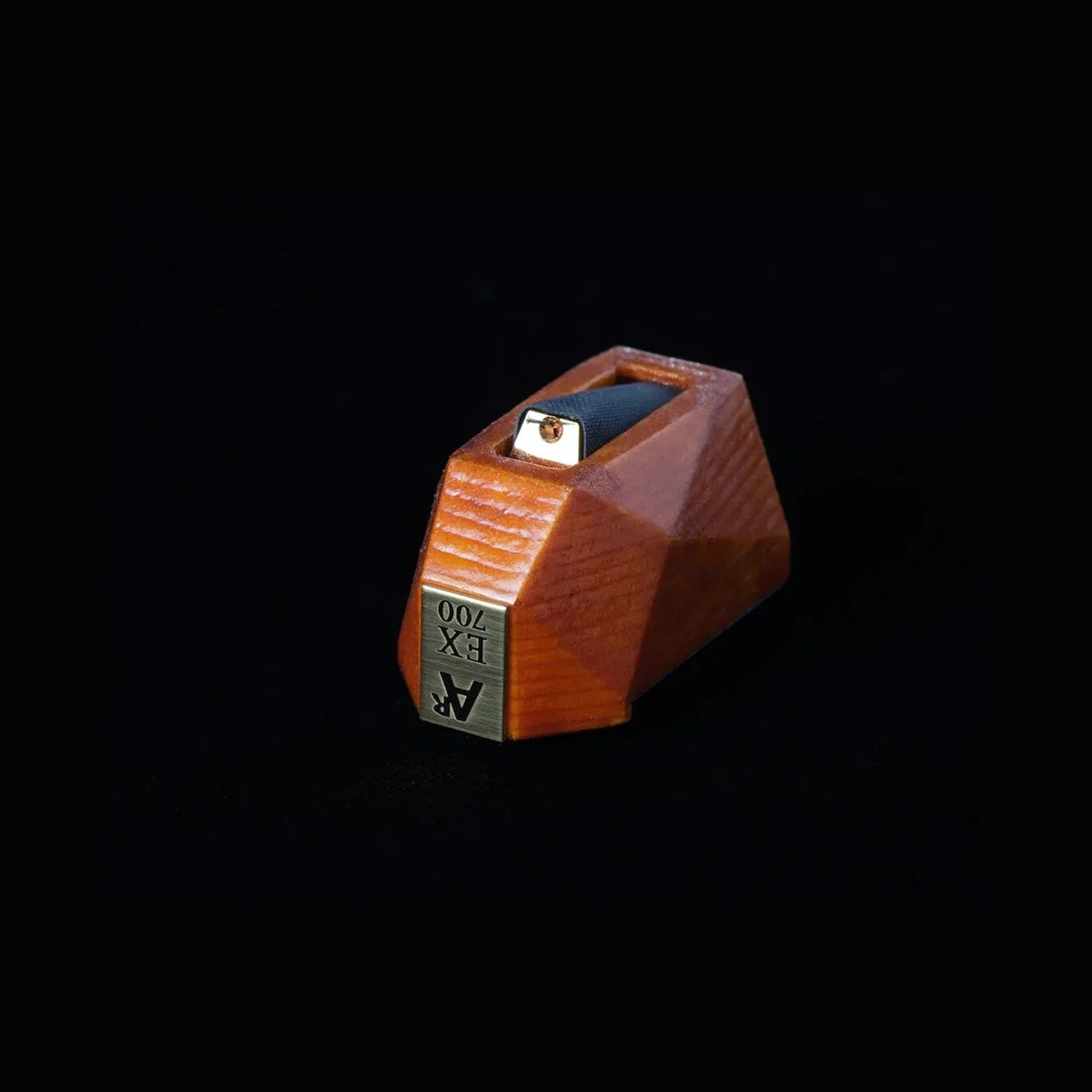 Wooden AR EX 700 phonograph cartridge stylus with a metal tip on a black background.