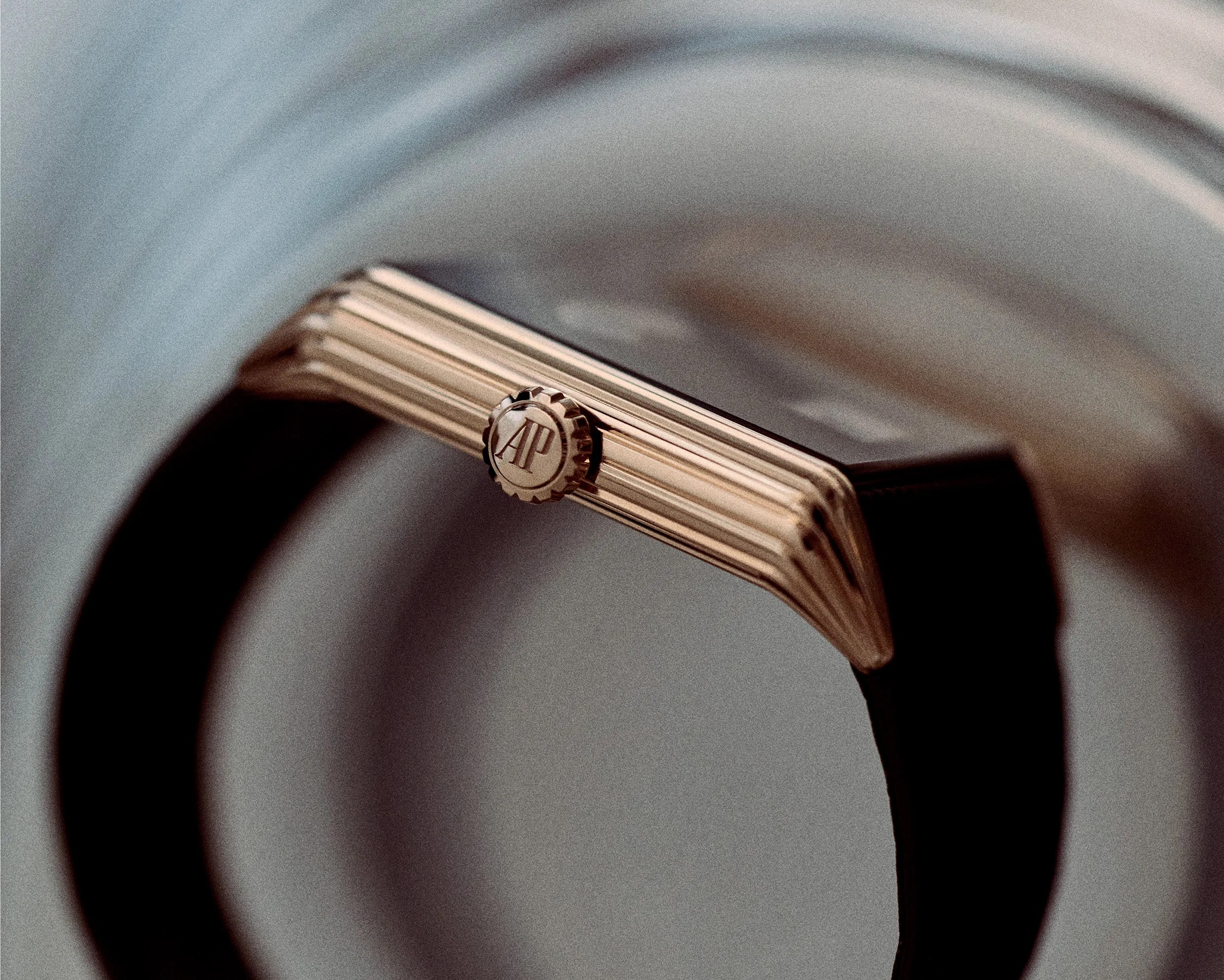 Close-up of a gold-toned watch crown with "AP" logo on a black strap.