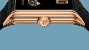 Close-up of a rose gold watch crown with "AP" logo on a black strap against a blue background.